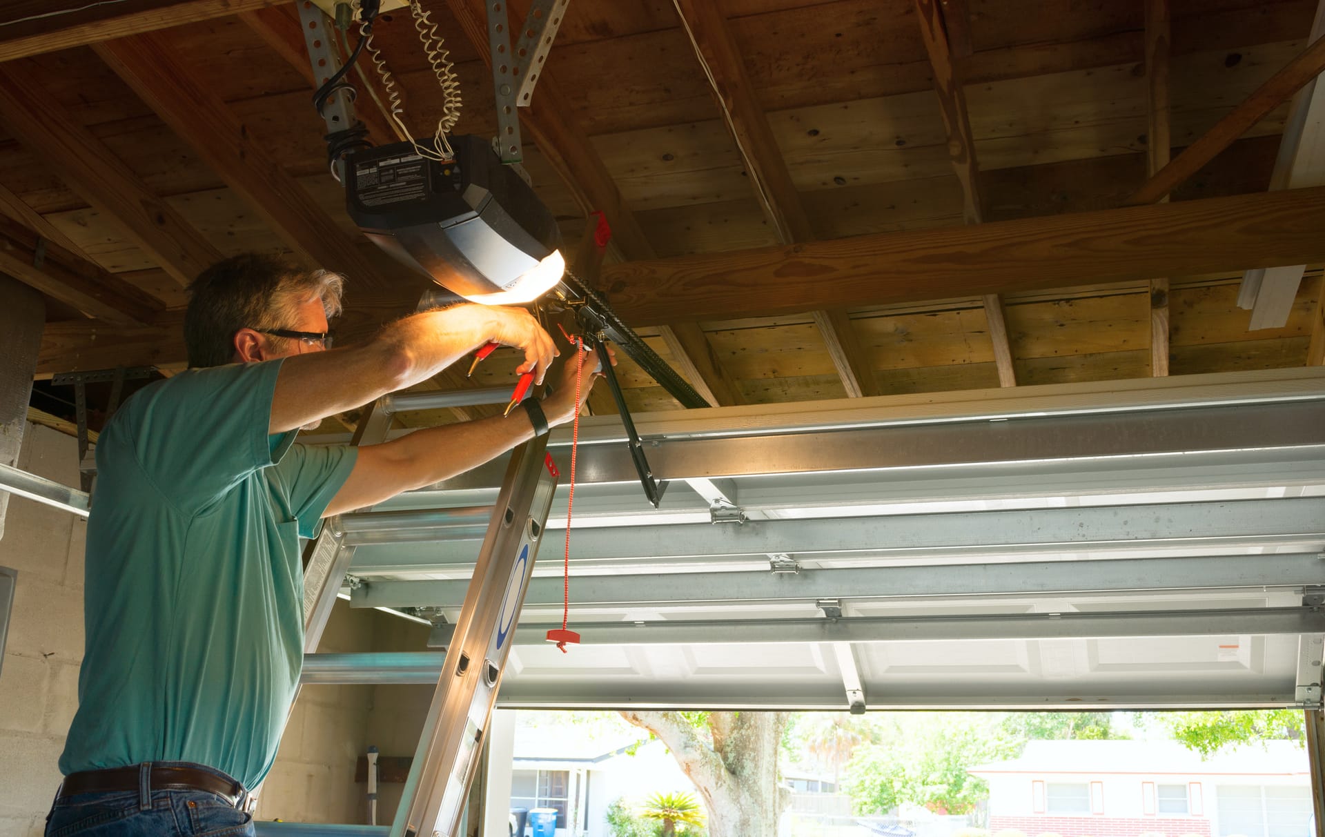 Technician on ladder installing garage door opener motor unit